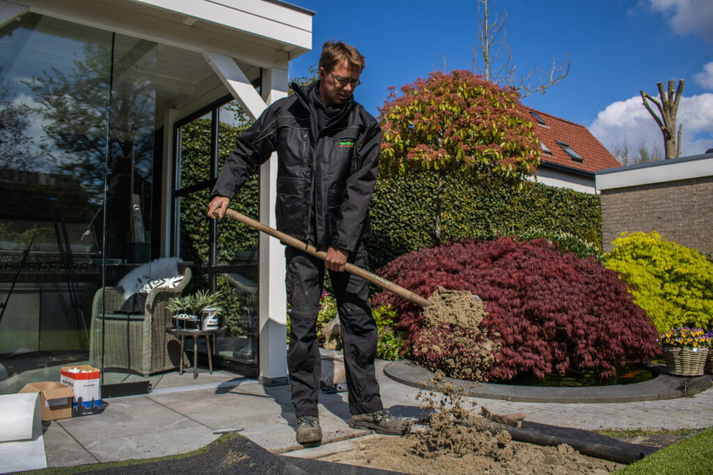 Het aanbrengen van een zandbed om het kunstgras uiteindelijk op aan te brengen.