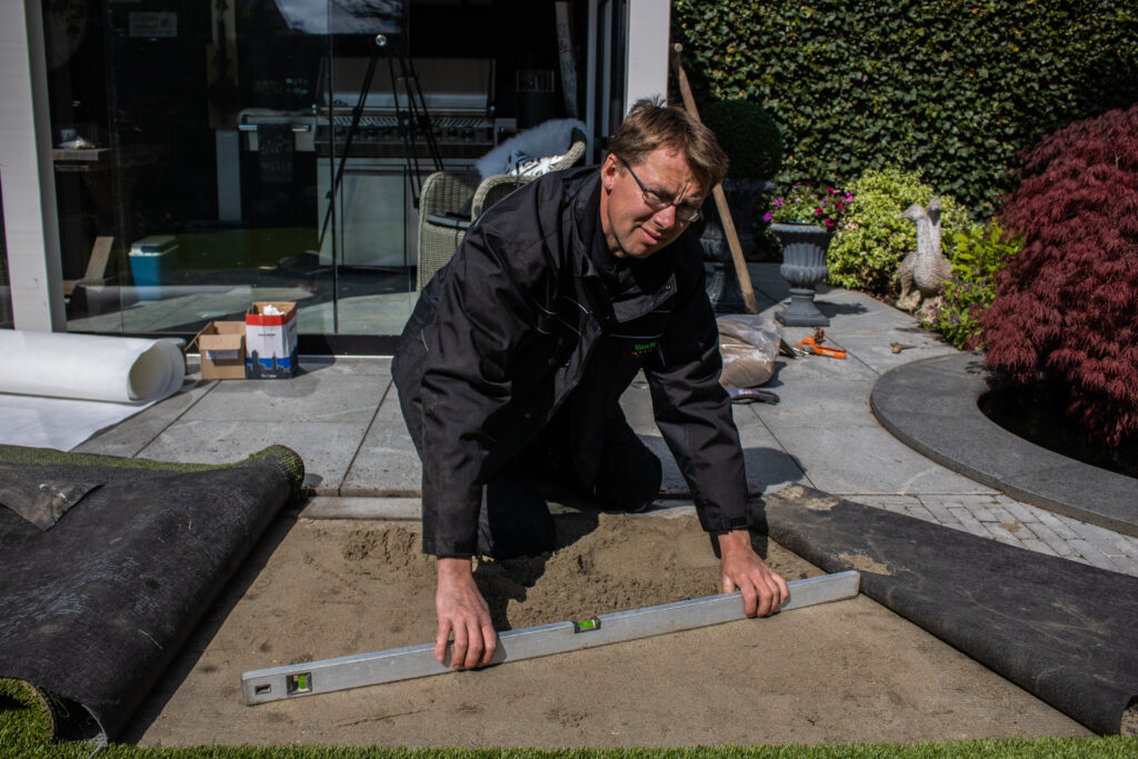 Het egaliseren van de onderlaag van zand met een waterpas.